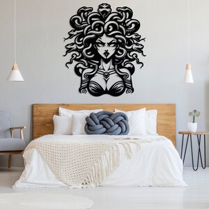 May include: Black and white metal wall art depicting Medusa, a mythical Greek figure with snakes for hair. The art is mounted on a white wall above a wooden headboard and white bedding.