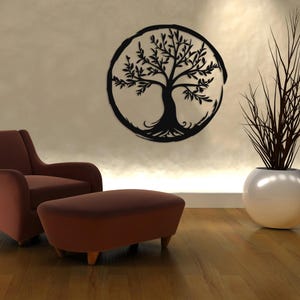 Peut inclure: Une sculpture murale en m&eacute;tal noir repr&eacute;sentant un arbre de vie avec des branches et des racines complexes, sur un mur beige. Un fauteuil et un pouf marron sont au premier plan, et une plante en pot se trouve &agrave; droite de l'image.
