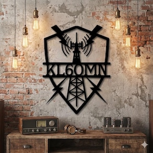 Peut inclure: Décoration murale en métal noir représentant une tour de radio avec le texte "KL60MIN". L'œuvre est fixée sur un mur texturé avec des briques apparentes. Des ampoules décoratives sont suspendues au plafond, éclairant la pièce.