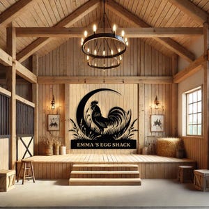 May include: A black metal sign featuring a rooster silhouette within a crescent moon and tall grass design. The text "EMMA'S EGG SHACK" is below the image. The sign is displayed on a wooden stage inside a barn.