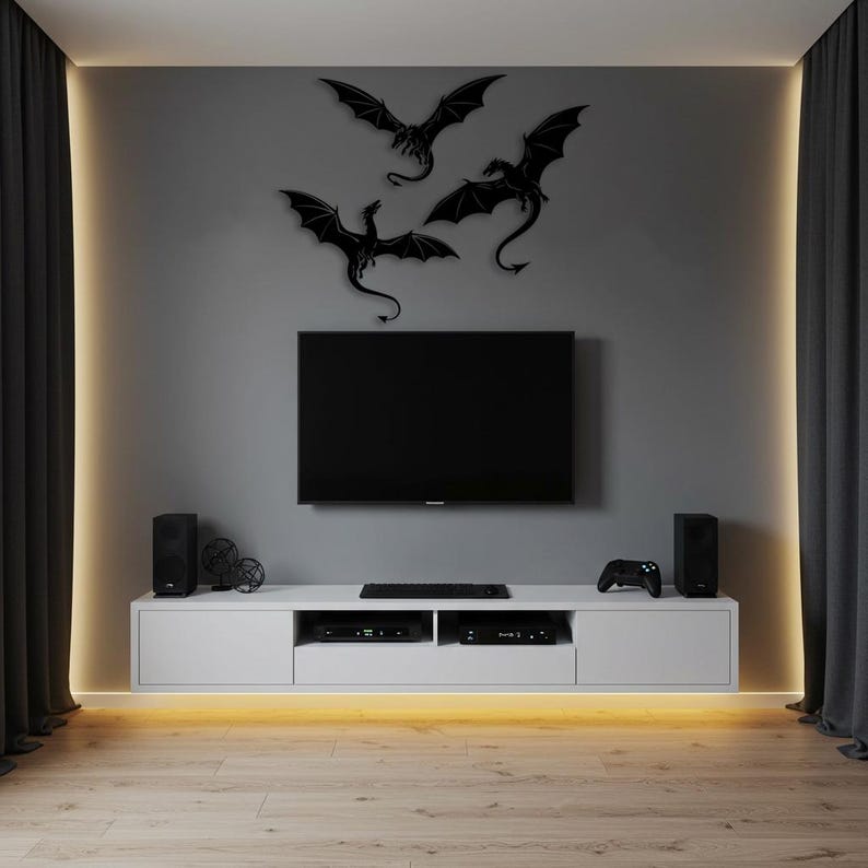 以下が含まれることがあります： グレーの壁に設置された大型フラットスクリーンテレビを備えたモダンなリビングルーム。テレビの上には、3つの黒いドラゴンのシルエットが表示されています。下の白いエンターテインメントユニットには、メディアコンポーネントが収納されています。スピーカーとゲームコントローラーも表示されています。