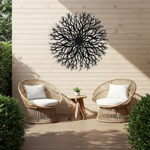 Puede incluir: Dos sillas de mimbre con cojines blancos y una peque&ntilde;a mesa de madera con una planta en maceta se encuentran en una terraza de madera frente a una pared de madera con una gran escultura de pared de metal negro en forma de sol.