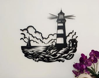 May include: Black metal wall art depicting a lighthouse with alternating white and black stripes, a small house, sailboat, and ocean waves. The artwork is mounted on a white wall, with purple orchids in the foreground.