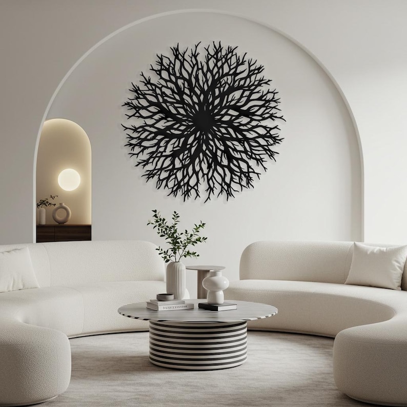 Puede incluir: Una escultura de pared de metal negro en forma de un gran &aacute;rbol circular ramificado. La escultura est&aacute; colgada en una pared blanca en una sala de estar moderna con un sof&aacute; blanco y una mesa de caf&eacute; a rayas blancas y negras.