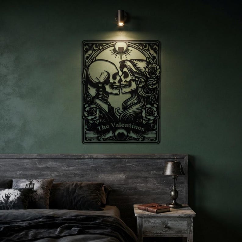 May include: A black metal wall art piece featuring a detailed illustration of two skeletons facing each other in a romantic pose, surrounded by roses and an ornate frame. The text The Valentines is centered at the bottom of the rectangular design.