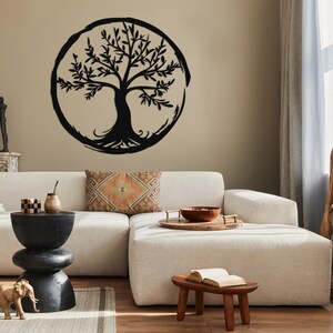 Peut inclure: Une d&eacute;coration murale en m&eacute;tal noir en forme d'arbre de vie avec un design circulaire. L'arbre est plac&eacute; sur un mur beige et est affich&eacute; au-dessus d'un canap&eacute; blanc avec un coussin &agrave; motifs bruns.
