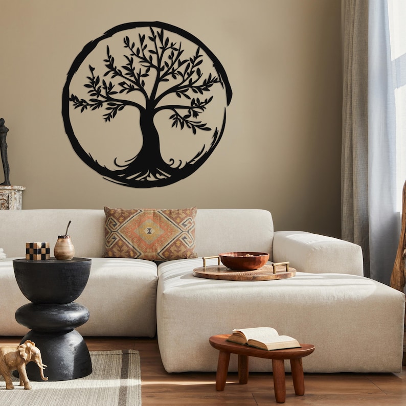 Peut inclure: Une d&eacute;coration murale en m&eacute;tal noir en forme d'arbre de vie avec un design circulaire. L'arbre est plac&eacute; sur un mur beige et est affich&eacute; au-dessus d'un canap&eacute; blanc avec un coussin &agrave; motifs bruns.