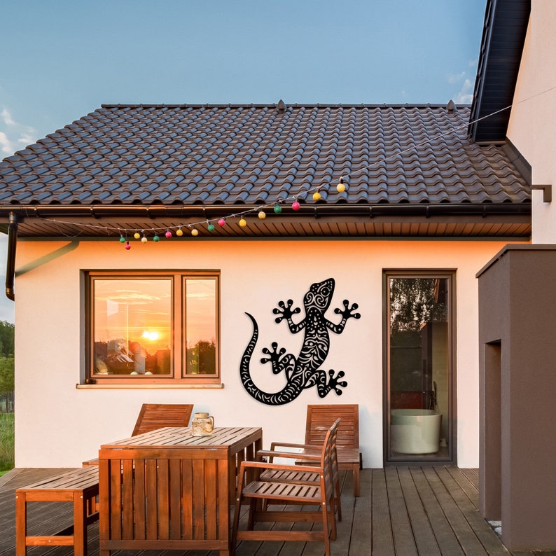 May include: Black metal gecko wall art with intricate details, mounted on a white wall of a modern home with patio furniture.