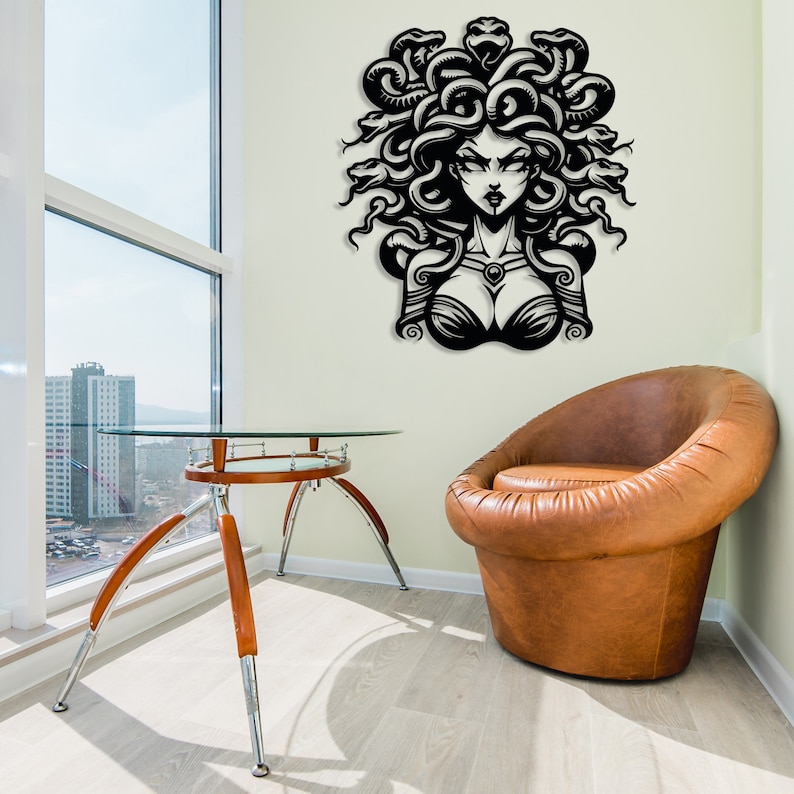 May include: Black and white wall decal of Medusa, a mythical Greek figure with snakes for hair, looking directly at the viewer. The decal is on a white wall in a room with a glass table and a brown leather armchair.