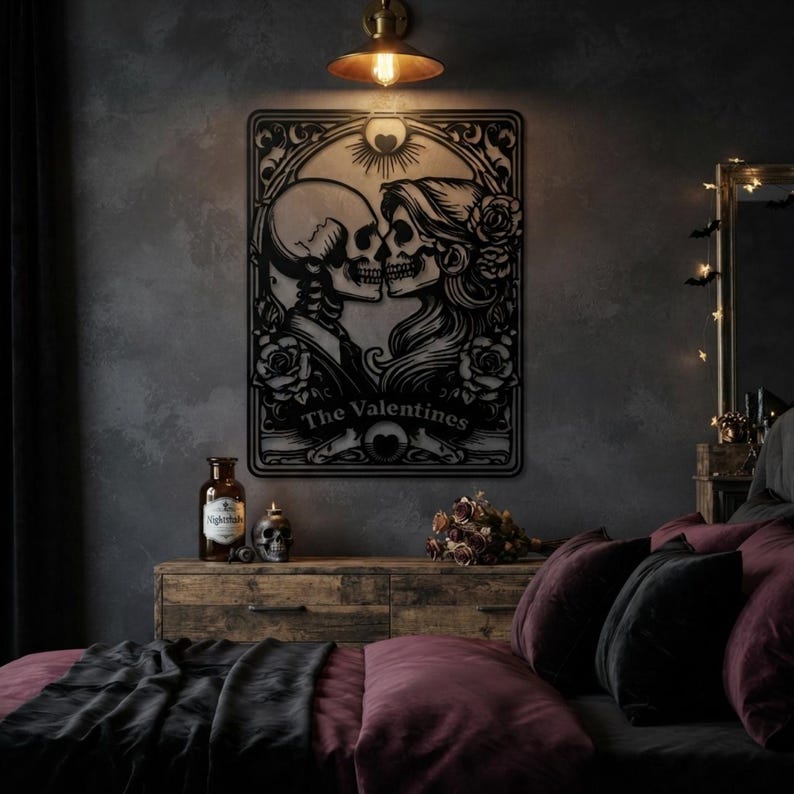 May include: A black metal wall art piece featuring a tarot card design with two skulls facing each other, surrounded by floral patterns and a sun motif. The text "The Valentines" is printed in a banner at the bottom of the rectangular frame.