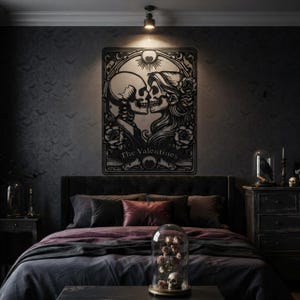 May include: A black metal wall art piece featuring a stylized illustration of two skulls facing each other, surrounded by roses and decorative filigree. The text "The Valentines" is printed at the bottom of the rectangular frame.