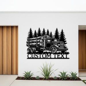 May include: Black metal wall art showing a vintage logging truck loaded with logs, with pine trees in the background. The words "CUSTOM TEXT" are below the truck. The artwork is mounted on a white wall.