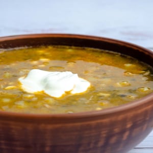 Peut inclure: Un bol brun rempli d'une soupe verte et jaune surmontée d'une cuillerée de crème fraîche blanche.