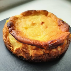 Könnte beinhalten: Ein runder, goldbrauner Käsekuchen mit leicht gebräunter Kruste. Der Käsekuchen hat eine glatte, cremige Textur.