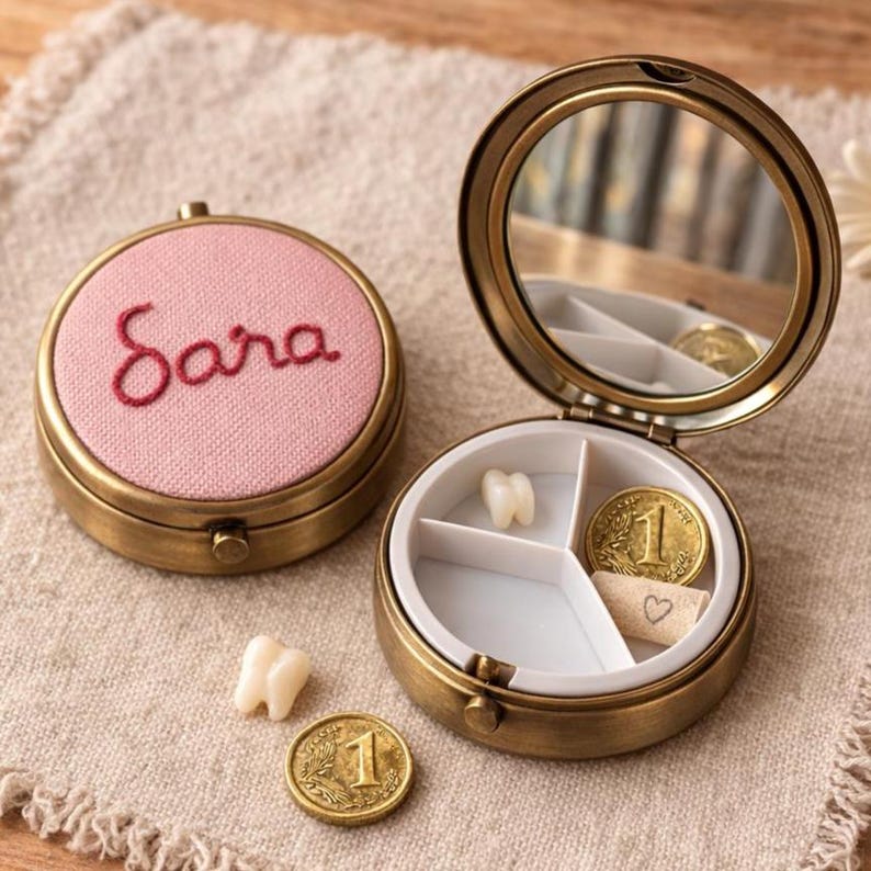May include: A vintage brass tooth fairy box with a pink lid embroidered with the name "Sara" in red thread. The open box reveals a mirror, a tooth, a coin, and a small paper with a heart.