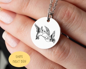 May include: A silver-colored necklace with a round pendant featuring a black and white illustration of three hummingbirds. The pendant is suspended from a delicate chain. The image also includes a yellow oval with the text "SHIPS NEXT DAY".