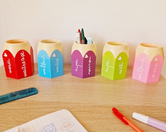 May include: Five colorful pencil-shaped desk organizers with different messages written on them. The messages are "merci", "maître d'ose", "meilleur maître", "super mignon", "super oesh" and "meilleure d'azam".