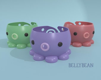 May include: Three octopus-shaped containers in green, purple, and pink. Each container has a large, round opening at the top and two black eyes. The containers are made of plastic and have a smooth, glossy finish.