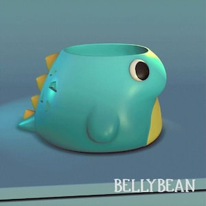 May include: A blue and yellow dinosaur-shaped ceramic planter with a single black eye. The planter is designed to hold small plants or succulents.