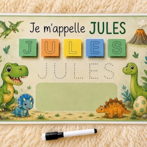 Peut inclure: Une fiche d'activité éducative rectangulaire avec le texte Je m'appelle JULES, des blocs de lettres colorés formant JULES, une ligne pointillée pour tracer le prénom, des illustrations de dinosaures, un volcan et un feutre effaçable.