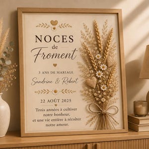 Peut inclure: Une affiche encadrée en bois clair avec le texte NOCES de Froment, 3 ANS DE MARIAGE, Sandrine & Robert, 22 AOÛT 2025 et un poème. Le design présente un arrangement floral en relief composé de blé séché, de marguerites et d'un nœud en ficelle.