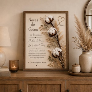 Peut inclure: Un cadre rectangulaire en bois contenant une impression couleur crème avec le texte "Noces de Coton 1 an de mariage Julia et Hugo Le 3 Août 2025" et un arrangement décoratif de fleurs de coton séchées et d'herbes beiges en relief.
