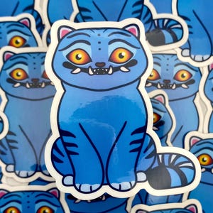 Puede incluir: Pegatina de gato azul con ojos naranjas y cola a rayas. La pegatina tiene un borde blanco y un diseño de dibujos animados. El gato tiene una expresión ligeramente gruñona y está rodeado de otras pegatinas similares.