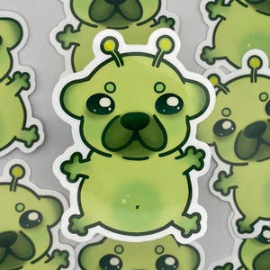 May include: A collection of green stickers featuring a cartoon pug with alien-like features. The pug has large, dark eyes, a green nose, and antennae. The stickers are outlined in white.