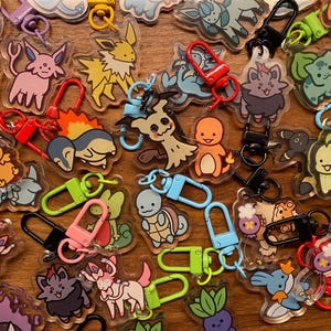 May include: A collection of colorful keychains featuring cartoon characters from the Pokemon franchise. The keychains are made of clear acrylic and feature various Pokemon, including Pikachu, Charmander, Bulbasaur, Squirtle, and more. The keychains are attached to metal rings and are perfect for adding a touch of fun to your keys or bag.