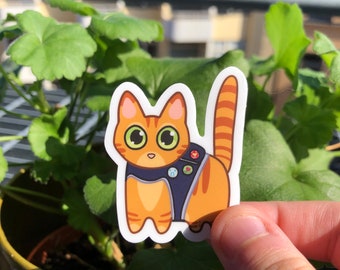 Puede incluir: Una pegatina de un gato atigrado naranja que lleva un chaleco azul con parches coloridos. El gato mira hacia la derecha con ojos grandes y redondos.