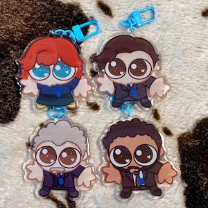 May include: Four cartoon character keychains with large eyes. The characters are wearing suits and have different hair colors. The keychains are made of clear plastic and have blue accents.