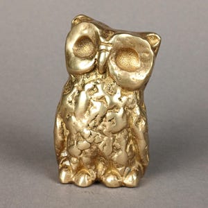 May include: A gold-colored owl figurine with a textured surface. The owl has large, round eyes and a slightly tilted head. The figurine is a decorative item, likely for home decor.
