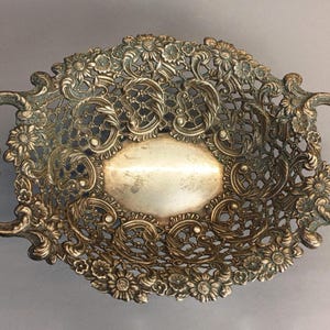 Könnte beinhalten: Verziertes silberfarbenes Serviertablett mit aufwendigen floralen und scrollartigen Details. Das ovale Tablett hat offene Seiten, eine ovale Mittelbasis und Griffe an jedem Ende. Ein dekoratives Stück zum Servieren oder Ausstellen.
