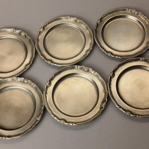 Puede incluir: Seis platos antiguos de tono plateado con bordes festoneados ornamentados. Los platos tienen un dise&ntilde;o simple y elegante, perfecto para cenas formales o exhibici&oacute;n. Cada plato tiene aproximadamente 23 cm de di&aacute;metro.