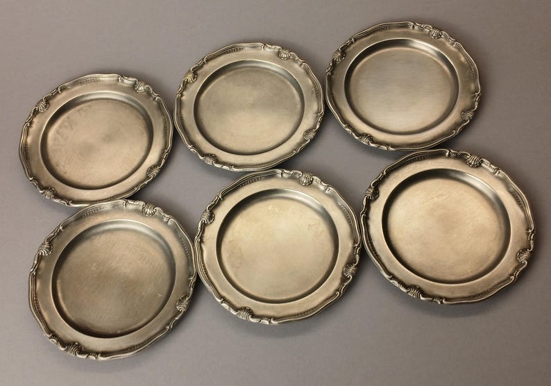 Puede incluir: Seis platos antiguos de tono plateado con bordes festoneados ornamentados. Los platos tienen un dise&ntilde;o simple y elegante, perfecto para cenas formales o exhibici&oacute;n. Cada plato tiene aproximadamente 23 cm de di&aacute;metro.