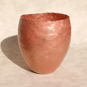Puede incluir: Jarrón de cobre martillado con superficie texturizada y forma redondeada. El jarrón, de color marrón rojizo, tiene una amplia abertura. Adecuado para la decoración del hogar, mide unos 20 cm de alto.