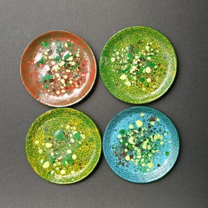 Puede incluir: Cuatro posavasos de cerámica coloridos con un diseño moteado. Los posavasos son rojo, verde, azul y amarillo con motas blancas.