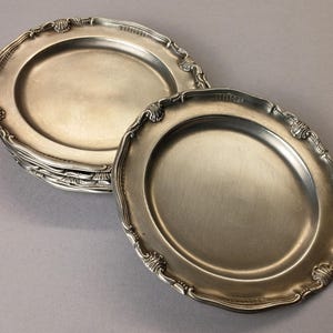 Puede incluir: Un conjunto de platos ovalados plateados antiguos con bordes festoneados ornamentados. Los platos tienen una superficie reflectante y est&aacute;n dispuestos sobre un fondo neutro. Los platos son probablemente para servir comida.