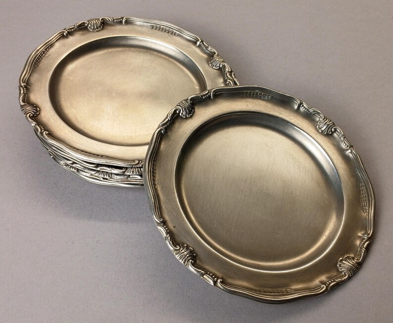Puede incluir: Un conjunto de platos ovalados plateados antiguos con bordes festoneados ornamentados. Los platos tienen una superficie reflectante y est&aacute;n dispuestos sobre un fondo neutro. Los platos son probablemente para servir comida.