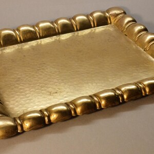 May include: A rectangular gold-colored tray with a hammered surface. The tray's border is adorned with a repeating, rounded design. The tray is likely made of metal and is suitable for serving or display.