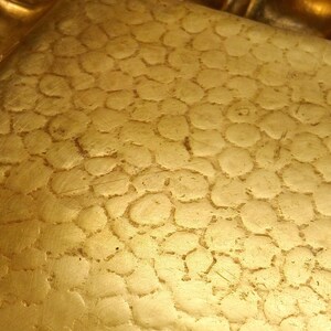 May include: Close-up of a gold-colored tray with a textured surface. The tray has a decorative, scalloped edge. The surface has a pattern of small, irregular circles.