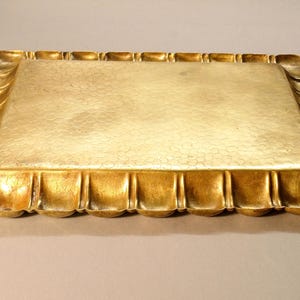 May include: A rectangular gold-colored tray with a textured surface and ornate, curved edges. The tray's border features a repeating pattern of rounded, vertical elements, adding a decorative touch to the serving piece.