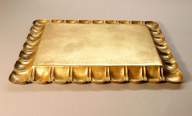 May include: A rectangular gold-colored tray with a textured surface and ornate, curved edges. The tray's border features a repeating pattern of rounded, vertical elements, adding a decorative touch to the serving piece.