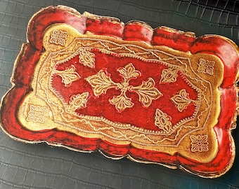 May include: A rectangular decorative tray with a red and gold ornate design. The tray features a central red panel with gold floral and leaf patterns, framed by a gold border and a red outer edge. The tray's edges are scalloped.