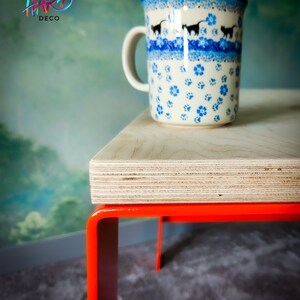 May include: A wooden table with orange metal legs. A blue and white ceramic mug with a cat design sits on the table.