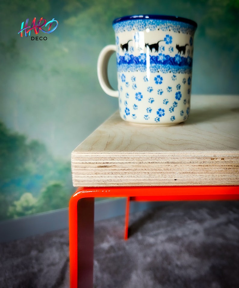May include: A wooden table with orange metal legs. A blue and white ceramic mug with a cat design sits on the table.