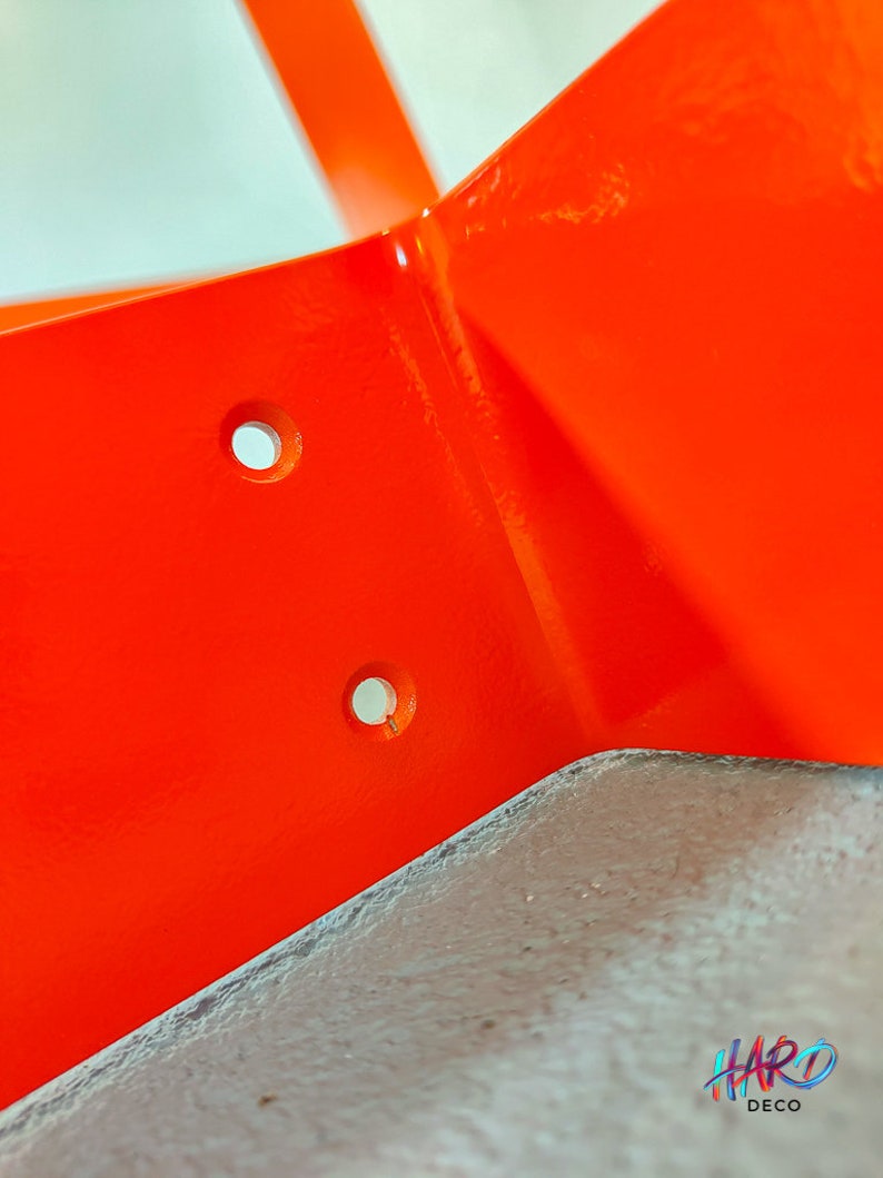 May include: Close-up of a bright orange metal corner bracket with two holes drilled into it. The bracket is painted a glossy orange.