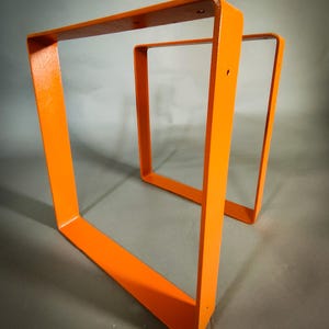 Op de afbeelding: Twee feloranje, vierkante metalen tafelpoten. De poten zijn gemaakt van dik metaal en hebben een gladde, glanzende afwerking. De poten zijn ontworpen om te worden gebruikt als basis voor een tafel of ander meubel.