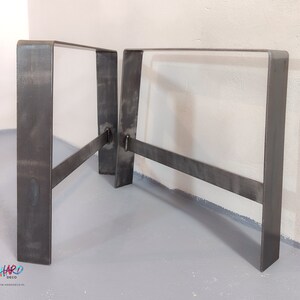 Puede incluir: Dos patas de mesa de acero en bruto con un diseño de marco rectangular. Las patas están soldadas con una barra transversal para mayor estabilidad. El metal tiene un acabado industrial oscuro. Las patas están diseñadas para soportar una mesa.