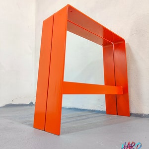 May include: A pair of orange metal A-frame stools. The stools are made of thick metal and have a simple, modern design.